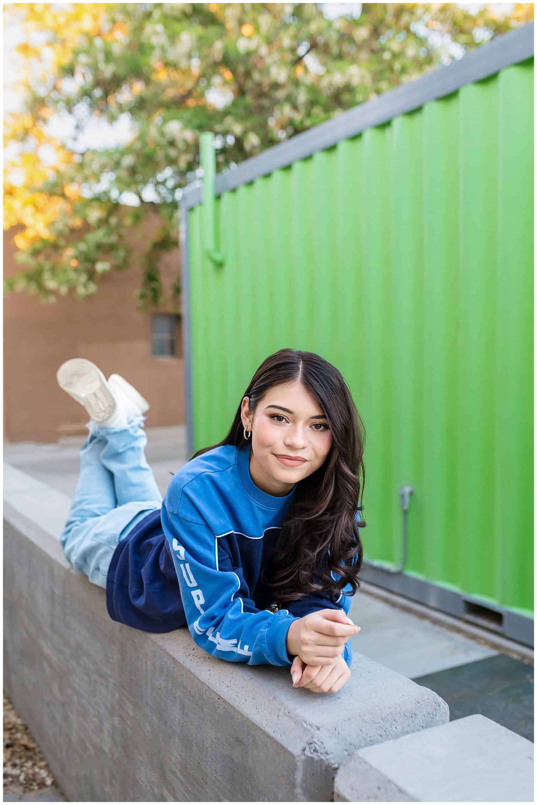 Class of 2025 senior striking a relaxed pose in casual jeans and a loose top in front of an industrial wall for senior pictures in Rio Rancho, New Mexico.