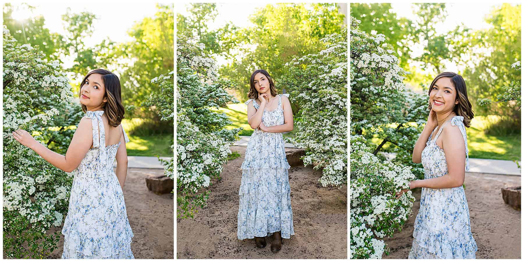 St. Pius senior wearing a white flowy dress with blue flowers and cowgirl boots in front of blooming white flower bushes at UNM.